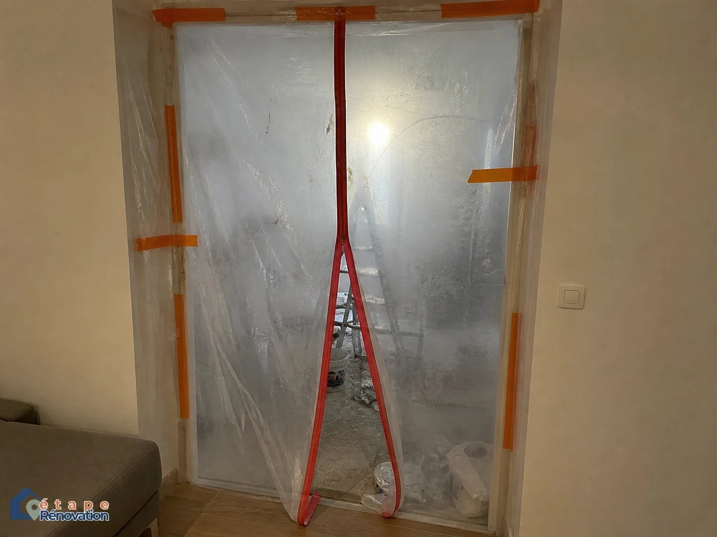 Chantier en site occupé : Une bâche de protection zippée sépare la zone de travaux du salon.